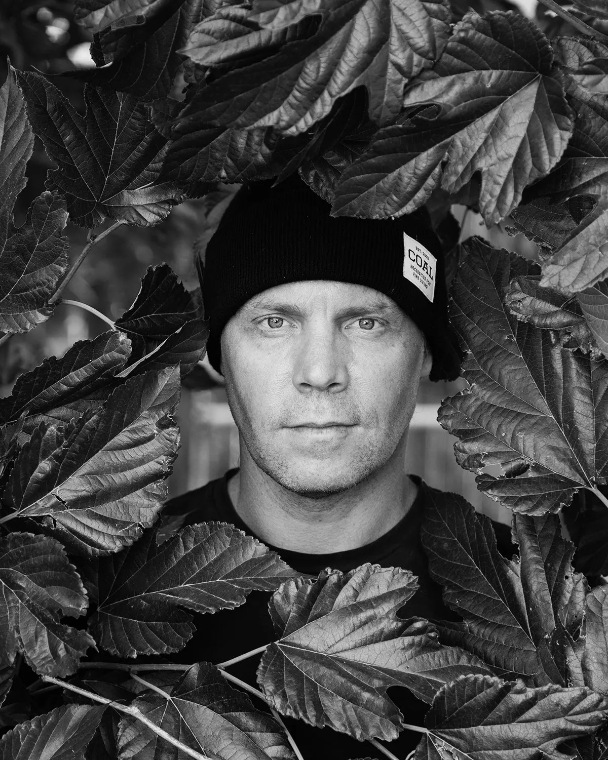 Black and white portrait of Travis Rice in a Coal beanie among leaves