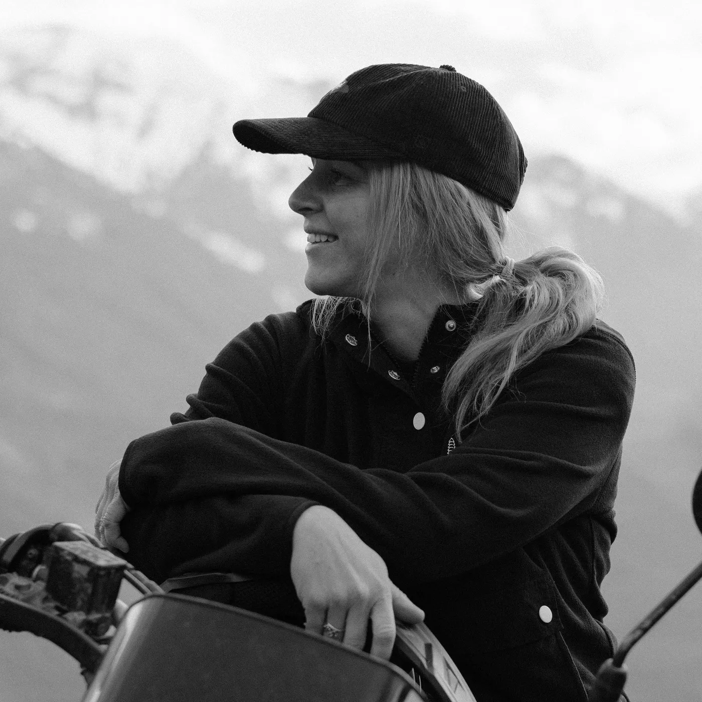 Black and white portrait of Darrah Reid in a cap with mountains behind