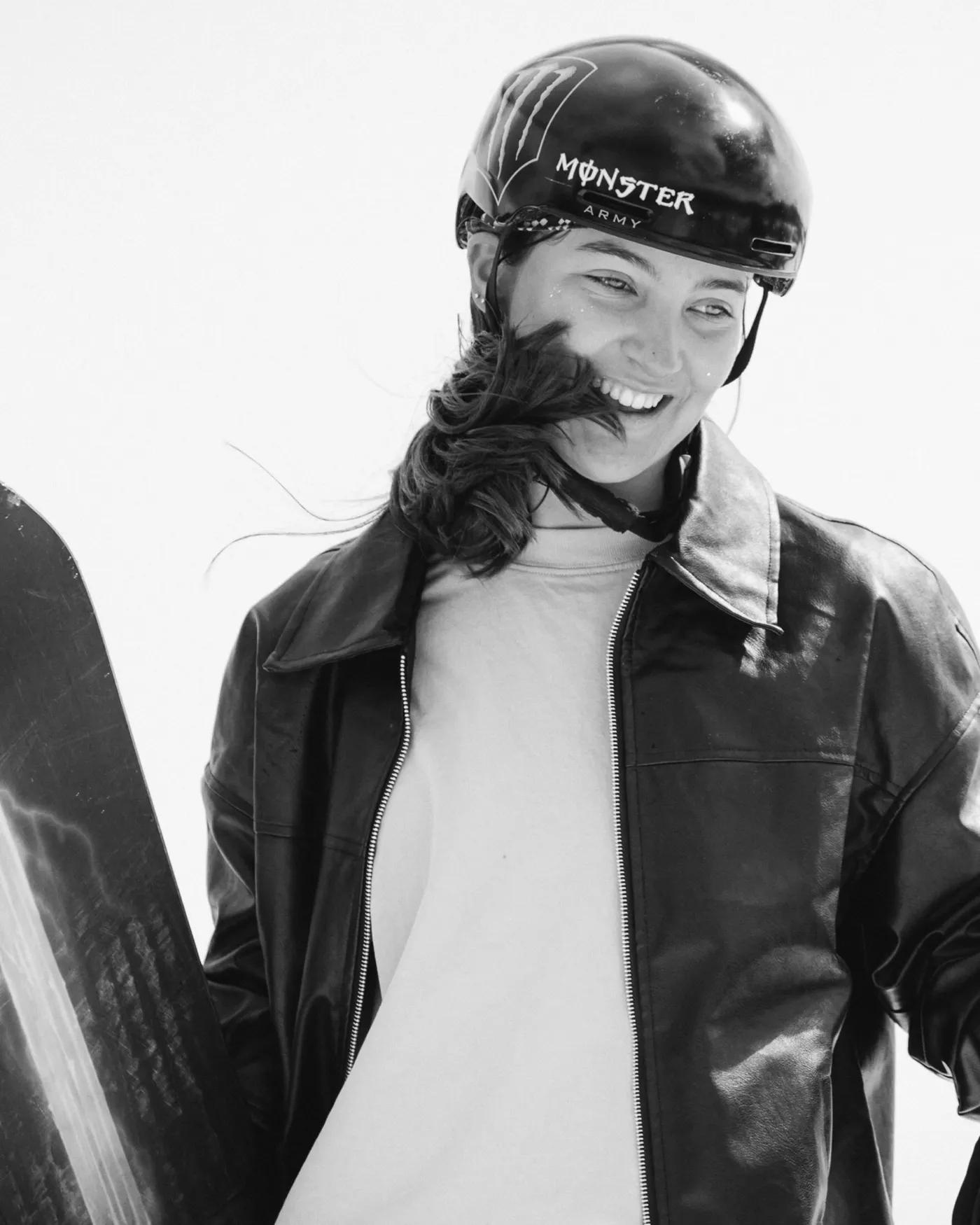 Black and white portrait of Jess Perlmutter laughing in a helmet with a snowboard