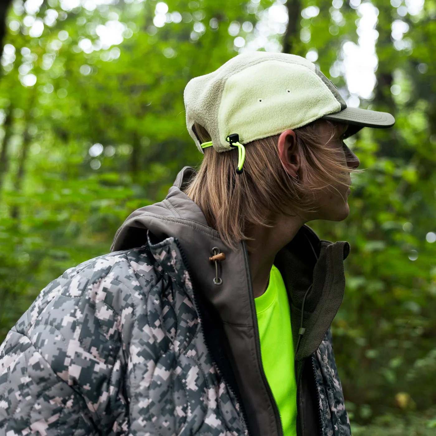 Person in a pale green Coal cap and a patterned jacket standing in a forest