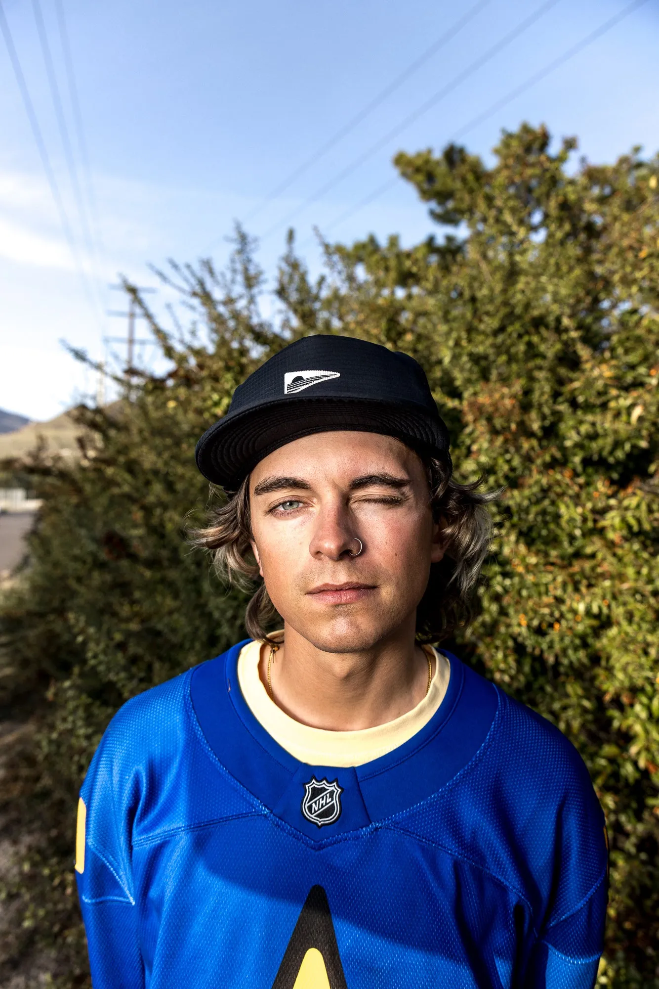 Young man in a black Coal cap and a blue jersey in front of a hedge