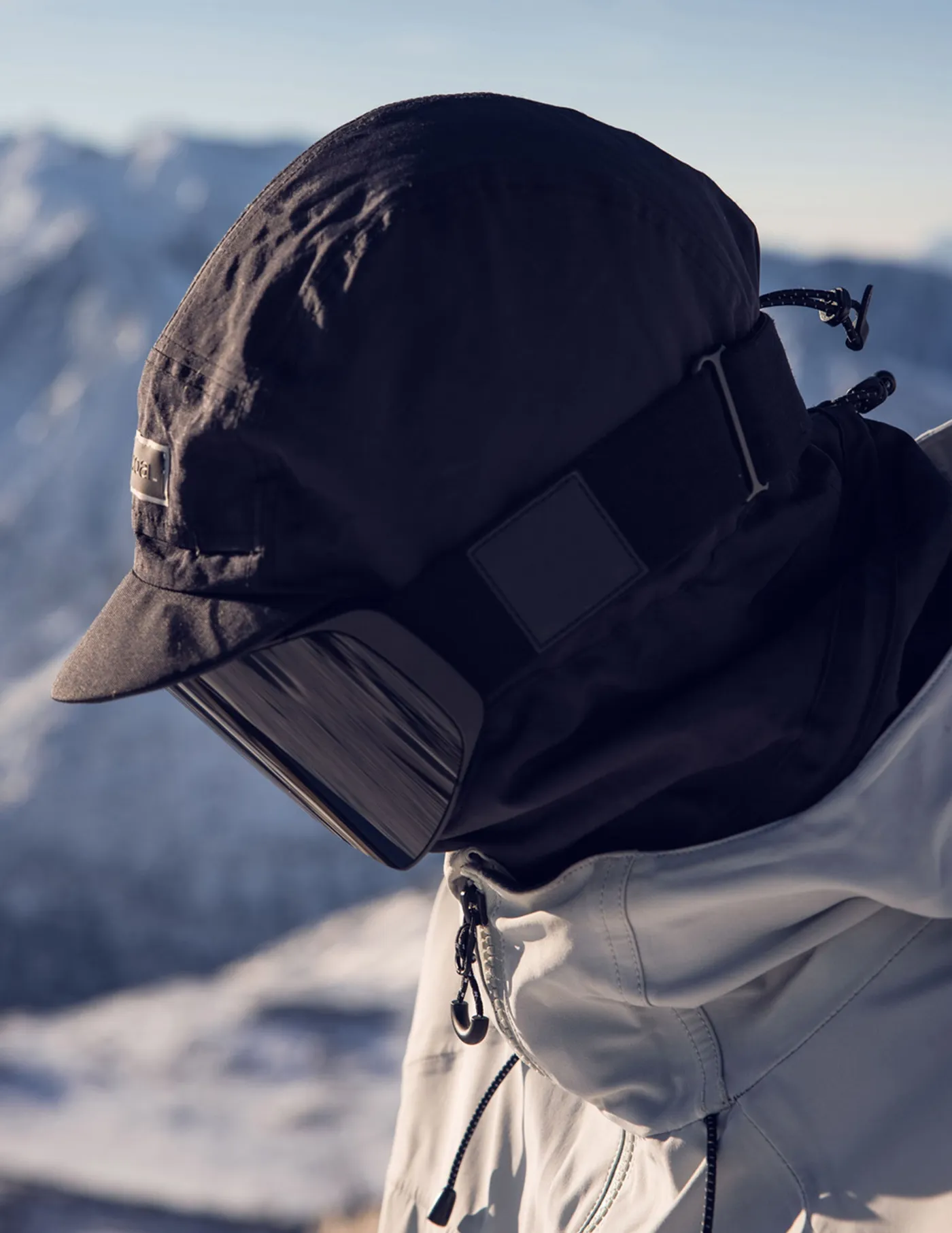 Rider in a black Coal hood and cap with snowy peaks behind