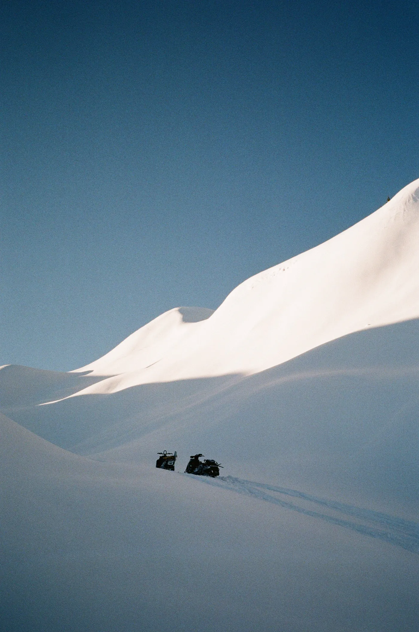 Two riders crossing a snow ridge under a dark blue sky