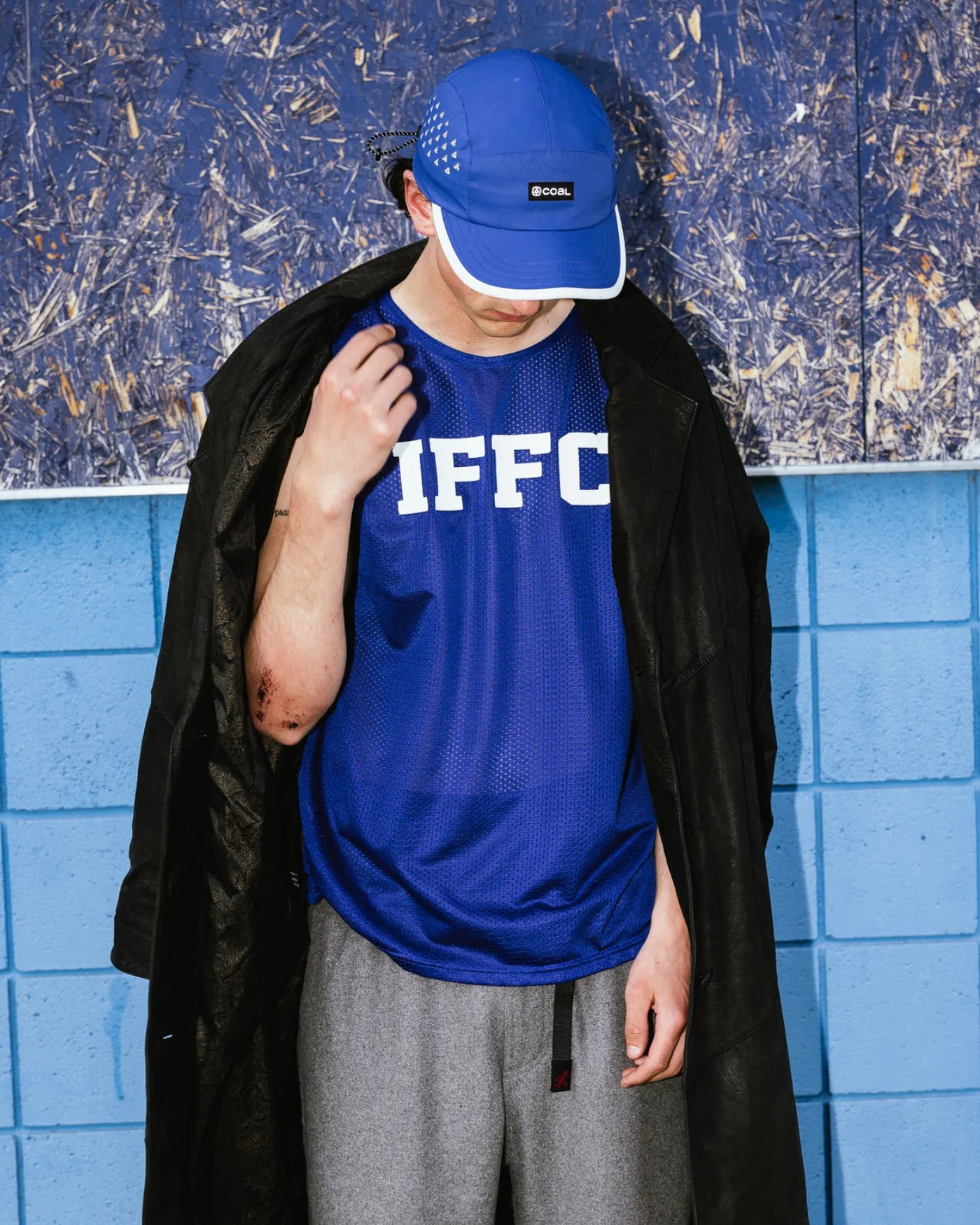 Man in a blue Coal cap leaning against a blue tiled wall in the city