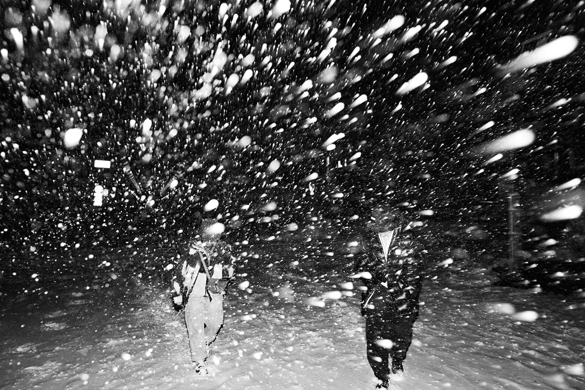 Black and white photo of two riders walking through heavy snowfall in Japan